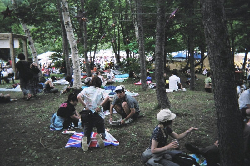 ワールド・レストランとレッド・マーキーの間にある木陰で休憩する人々。 