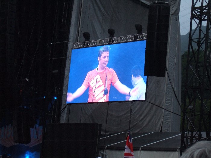 スタッフTシャツを着て公演するカイザー・チーフスのボーカル。