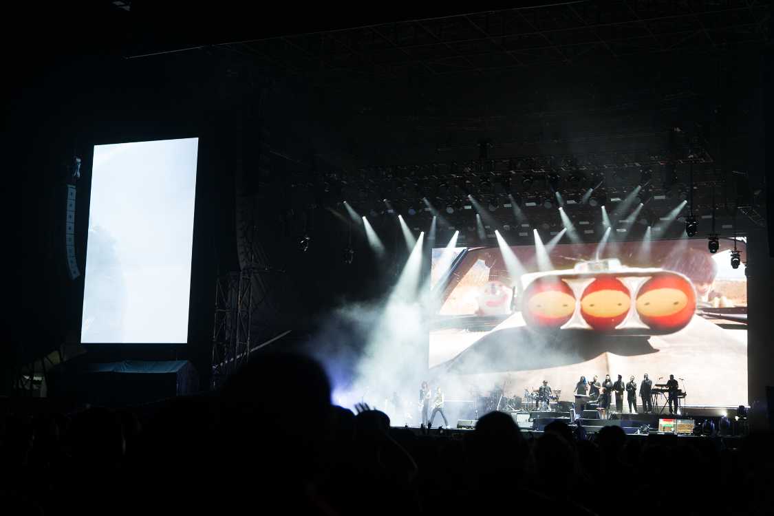 コーラスが6人並び、ギター、ベース、キーボード、ドラム、パーカッション、シンセサイザーがいます。