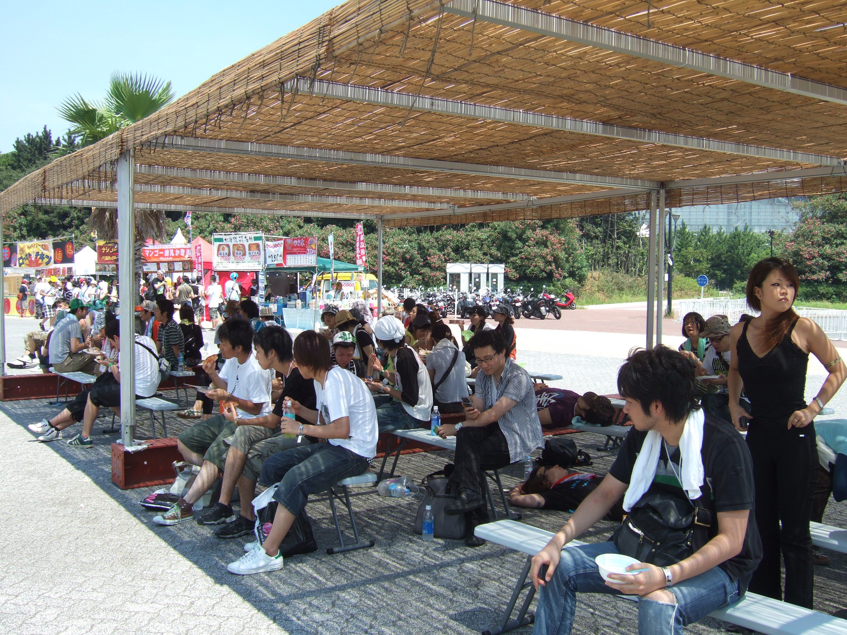 フジロックフェスティバルに比べ、コンクリート、アスファルトの照り返しが厳しい、木陰がほとんどない、などで、外は直射日光を避ける場所があまりありません。幕張メッセへ行けば全体が室内になりますが、遠いので、食事を取る場所を兼ねて設置されたと思われます。陰さえあればテントである必要もありません。 